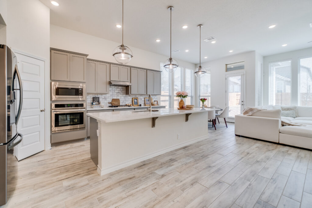 Completed new kitchen build by Black Ridge Contracting in Des Moines Iowa with gray cabinets quartz countertops island pendant lights and open floor plan to living room